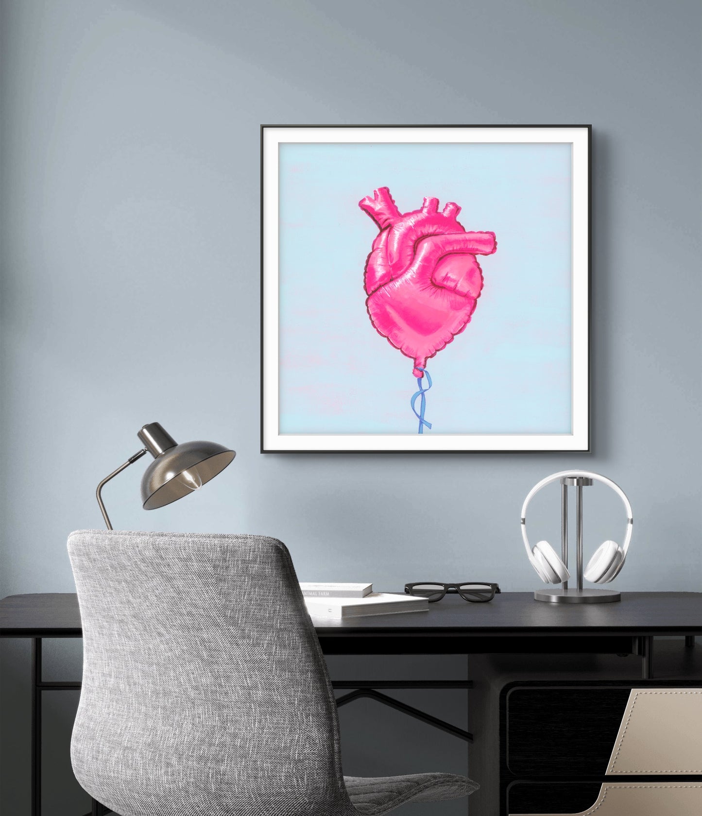 Framed artwork of a pink heart-shaped balloon on a gray wall above a desk.
