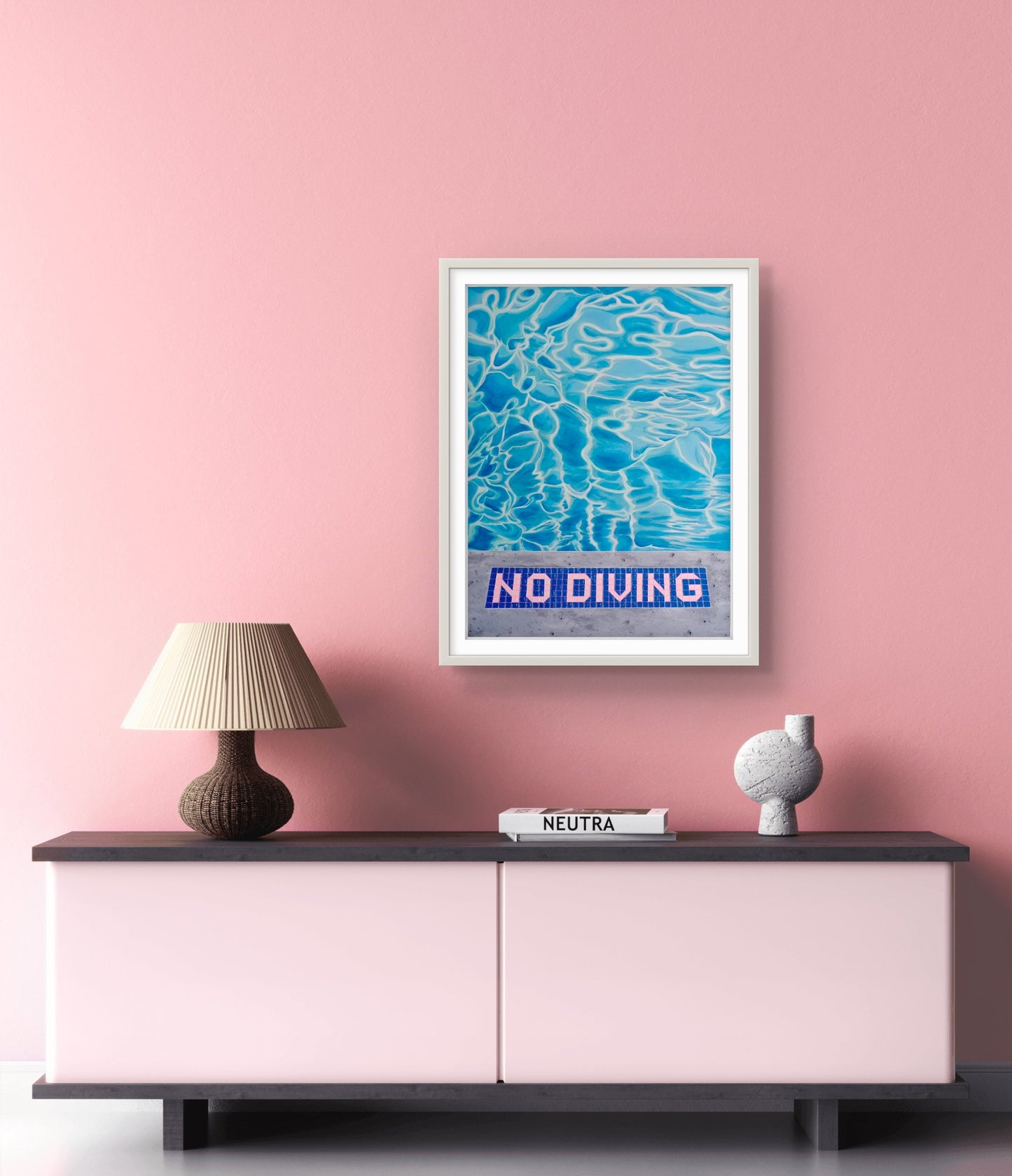 Framed 'No Diving' artwork on a pink wall above a sideboard with decor items.