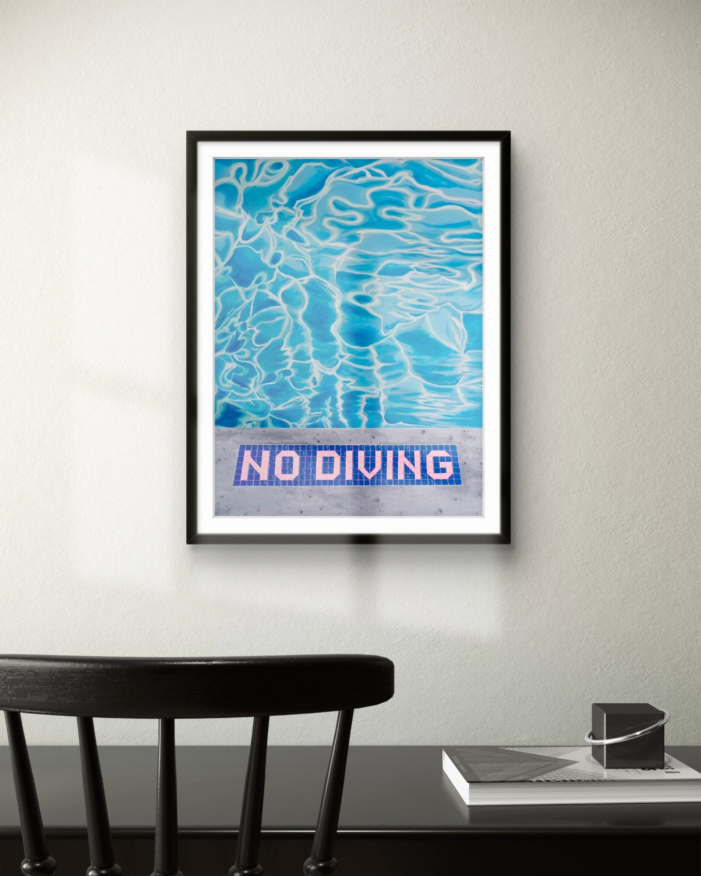 Framed artwork with blue water pattern and 'No Diving' text on a wall above a desk.