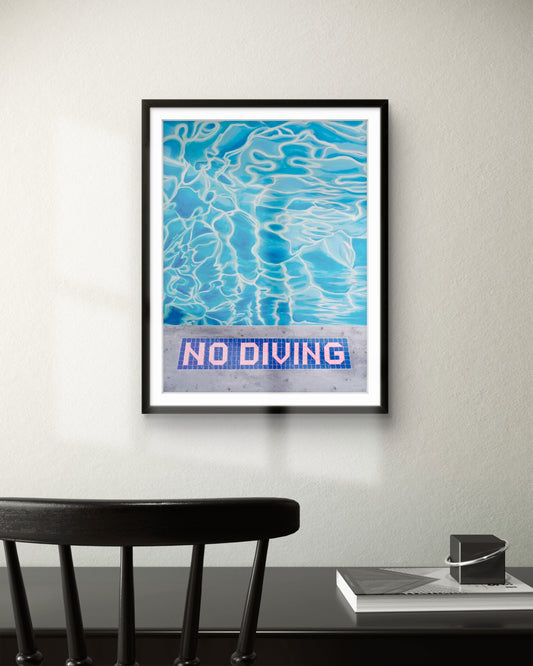 Framed artwork with blue water pattern and 'No Diving' text on a wall above a desk.