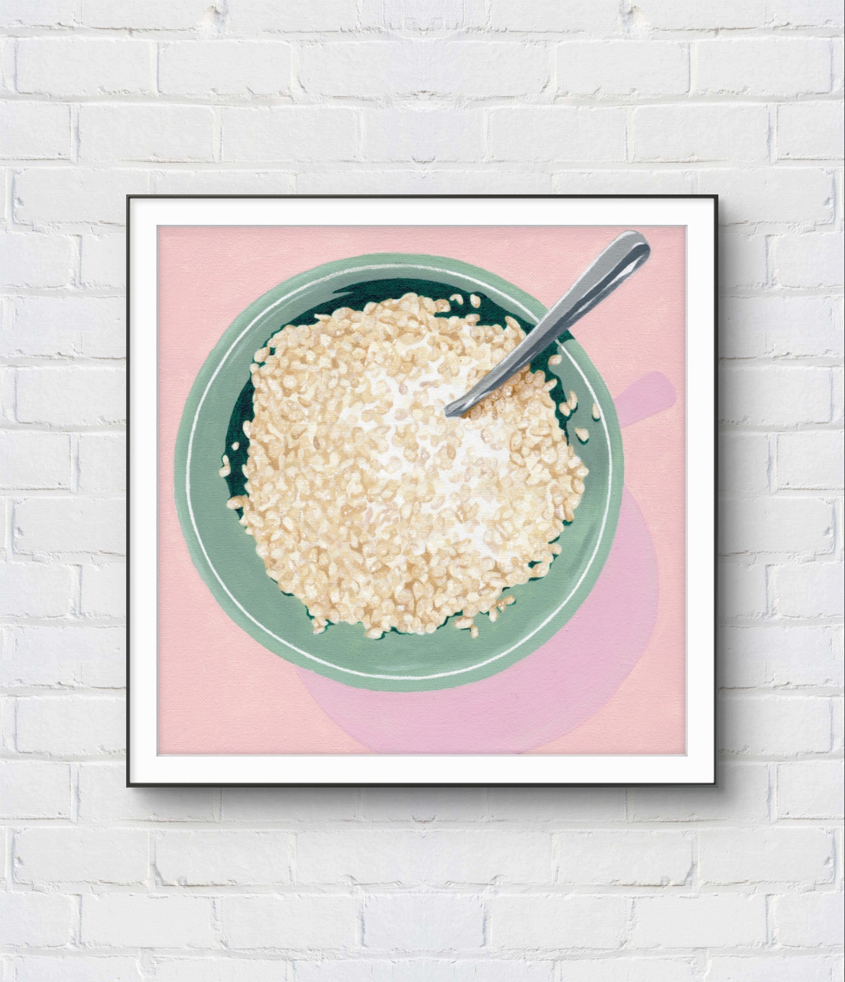 Framed artwork of a bowl of cereal with a spoon on a pink background, mounted on a white brick wall.