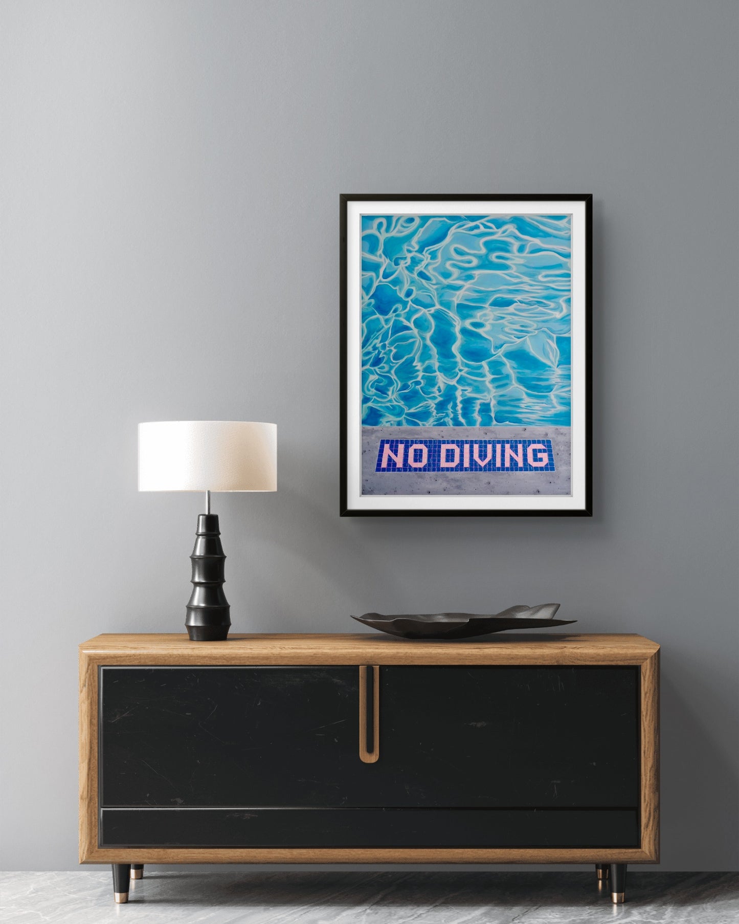 Framed 'No Diving' poster above a wooden console table with a lamp and decorative bowl.